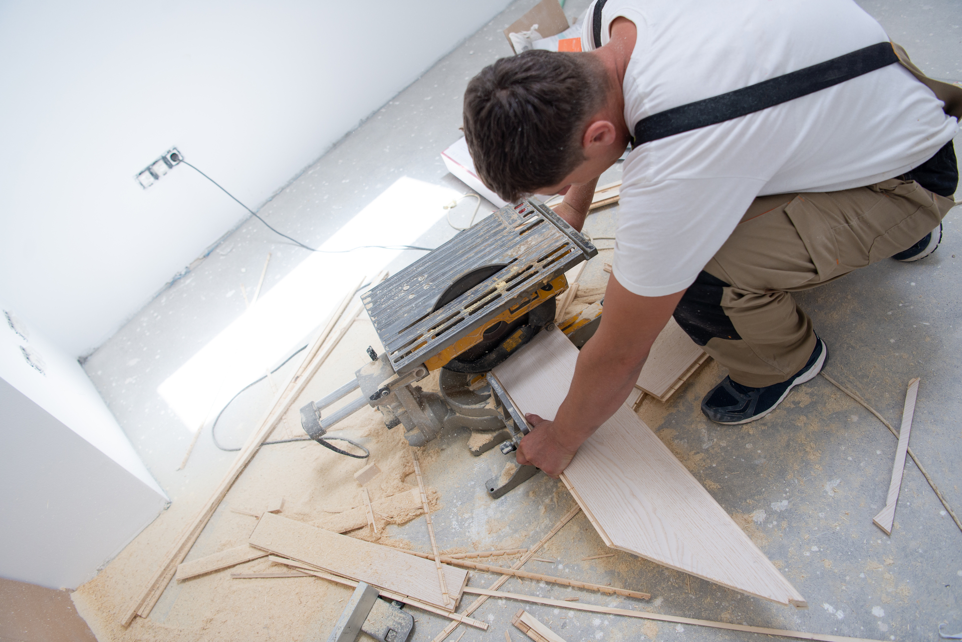 Man cutting laminate floor plank with electrical circular saw